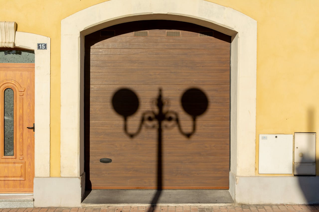 Wooden door and garage with streetlamp shadow on a sunny city street.