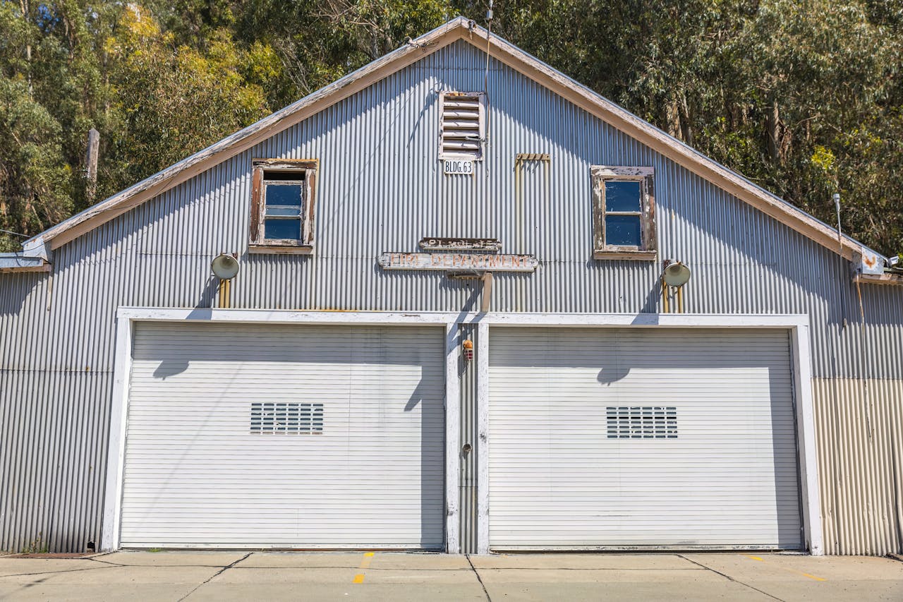 A sunlit vintage metal garage with double doors and rustic charm amidst trees.