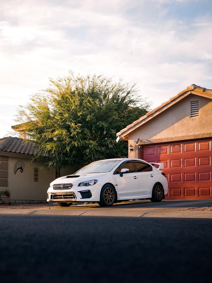 White car parked in a suburban driveway beside a red garage under a clear sky.