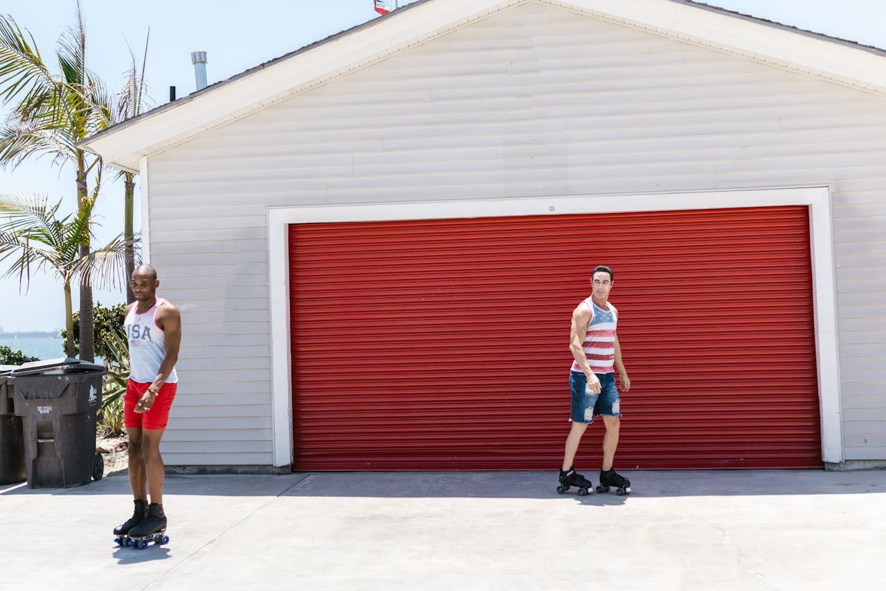 Two men enjoying a sunny day roller skating in front of a red garage door, creating a sense of leisure and fun.